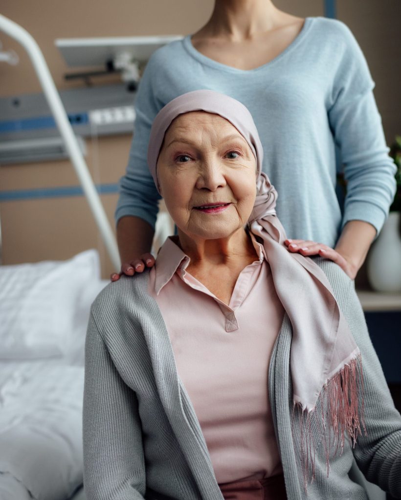 smiling senior woman in kerchief looking at camera with daughter on background in hospital